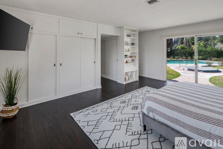 A bedroom with a large bed and a pool outside the window.