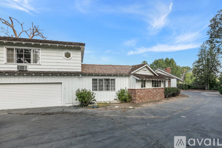 A white building with a grey roof and a tree in front of it.