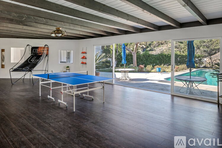 A ping pong table is in the middle of a room with a pool table and a slide.