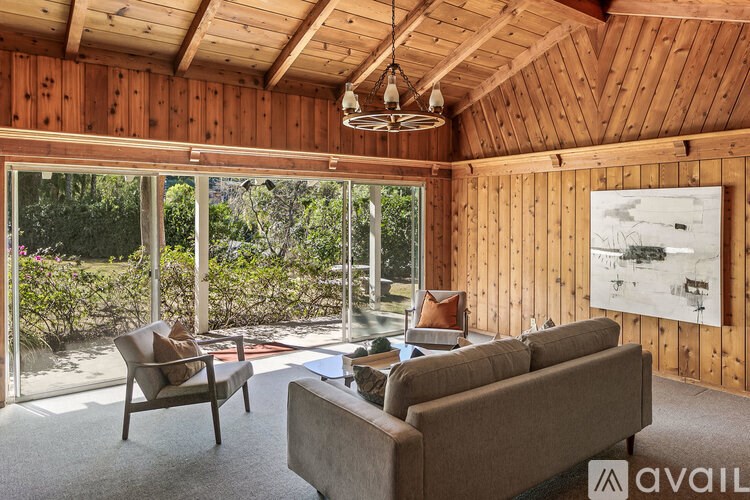 A living room with wooden walls and a large window overlooking a garden.