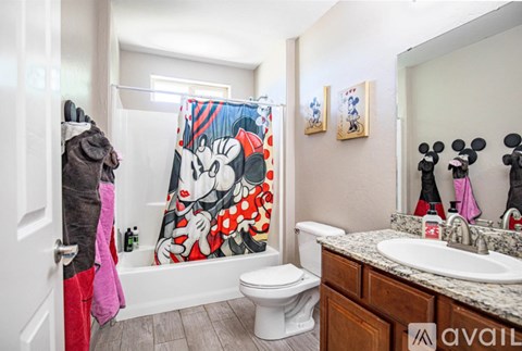 A bathroom with a toilet, sink, and a shower curtain with Mickey Mouse on it.