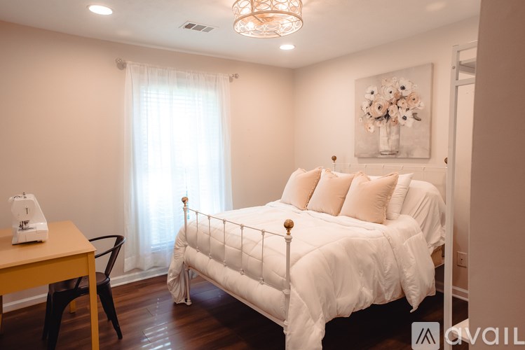 A white bed with a white comforter and pillows in a room with a wooden table and chair.
