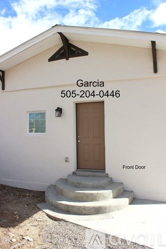 A white house with a brown front door and a window on the left.