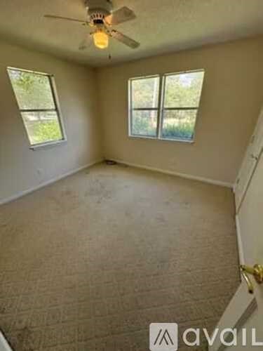 A room with a ceiling fan and two windows.