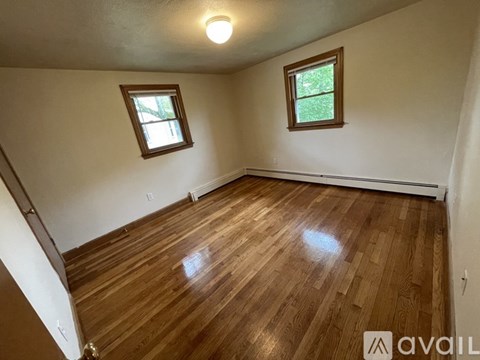 A room with wooden flooring and two windows.
