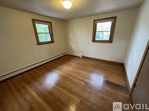 A room with wooden flooring and two windows.