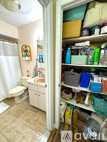 A bathroom with a toilet, sink, and a cabinet full of items.