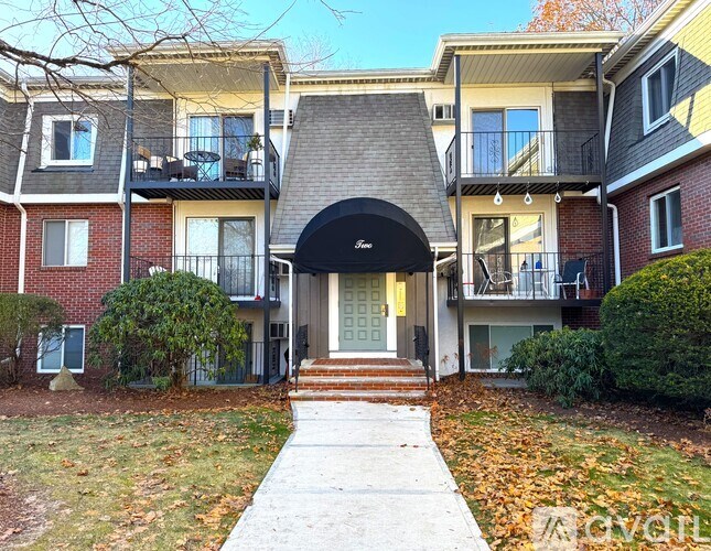 A building with a black awning and a white door is surrounded by bushes and trees.