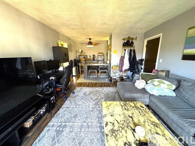 A living room with a grey couch, a yellow patterned coffee table, and a black television.