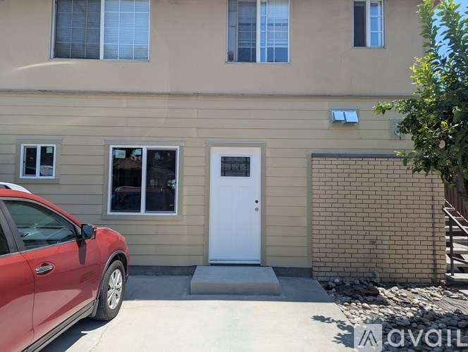 A red car is parked in front of a beige house.