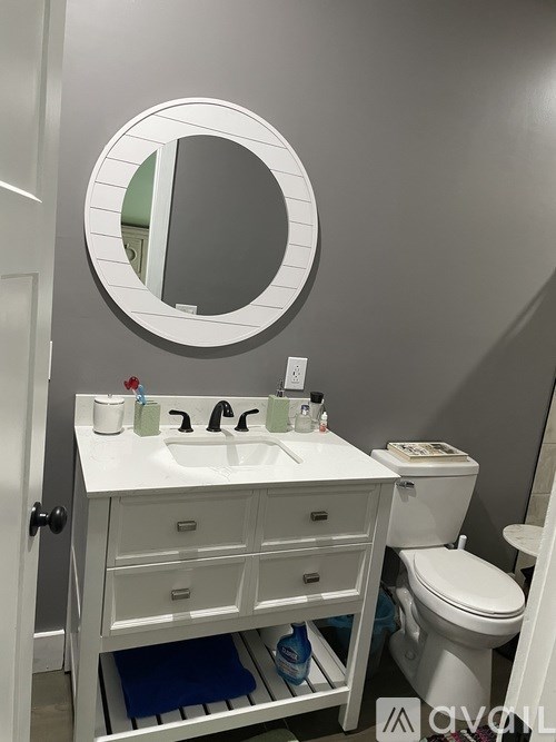 A white bathroom with a round mirror and a white sink.