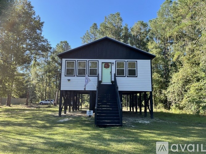 A small house with a porch and a red door is surrounded by trees.