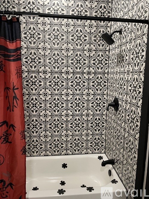 A shower with a red curtain and a black and white tiled wall.