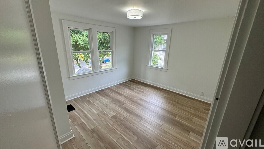 A room with wooden flooring and two windows.