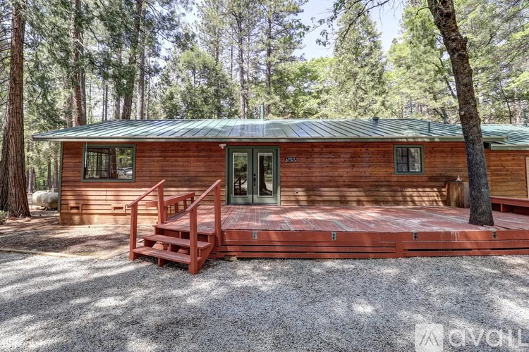 A wooden cabin with a green roof is surrounded by trees.