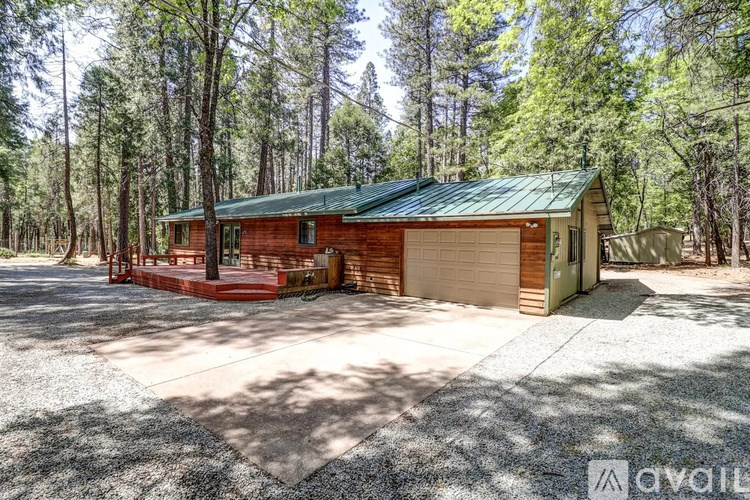 A house with a green roof is surrounded by trees and has a gravel driveway.