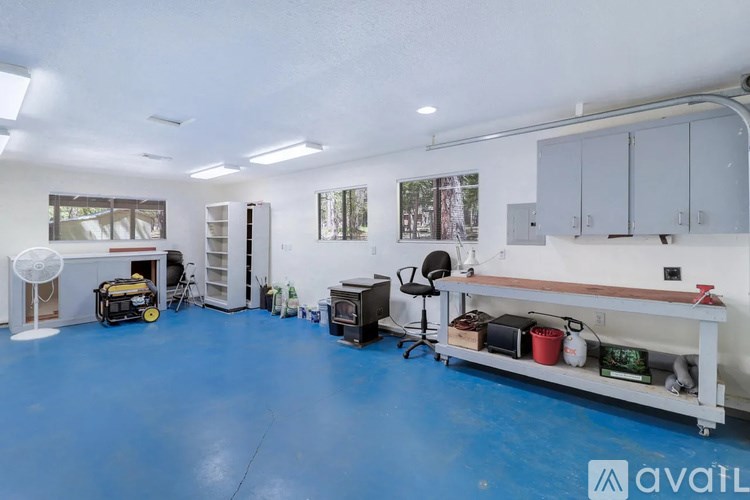 A room with a blue floor and white walls, containing a workbench, cabinets, and various items.