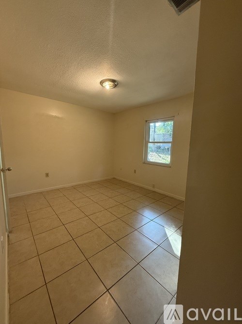 A room with beige walls and tile flooring with a window.
