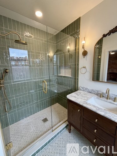 A bathroom with a green tiled shower and a marble countertop.