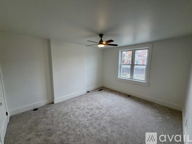 A room with a ceiling fan and a window with a view of a building outside.