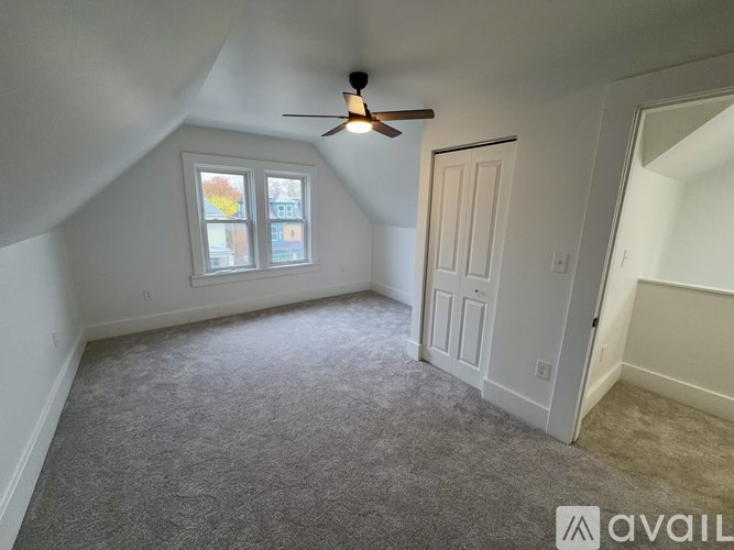 A room with a ceiling fan and a window with a view of a street.