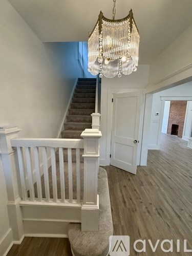 A chandelier hangs over a staircase with white railings and a beige carpet.