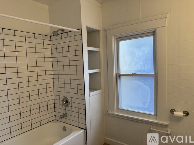 A bathroom with a white tub, a window, and a toilet paper roll.
