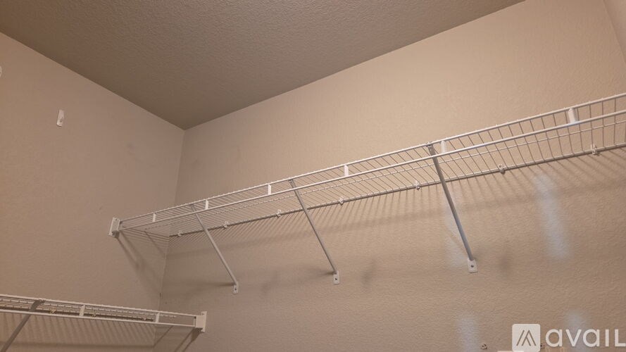 A white shelf with a metal rod is mounted on a white wall.