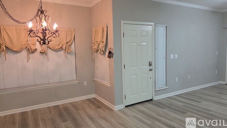 A room with a chandelier, a door, and a window with curtains.