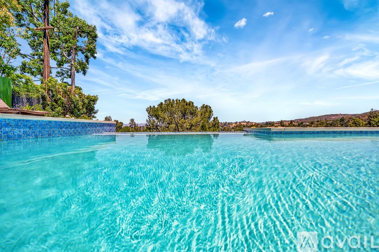 A clear blue swimming pool with a view of the sky and trees.