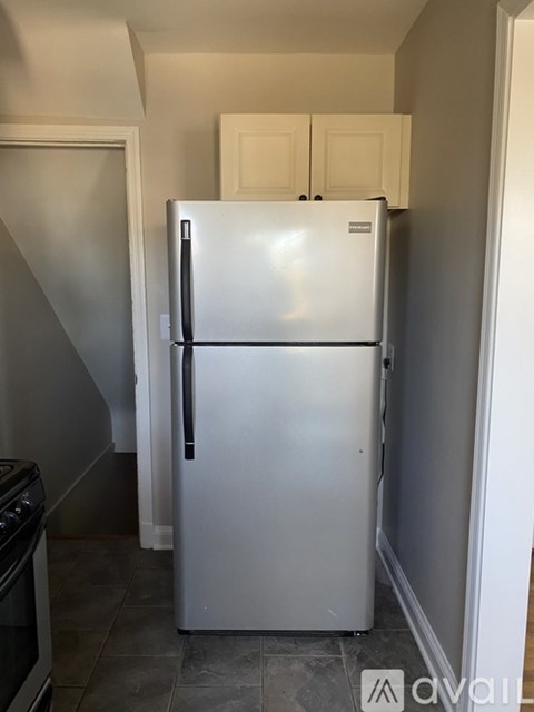 A white refrigerator in a kitchen with a stove top oven to the left.