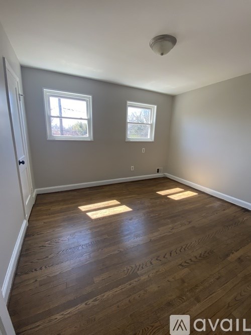 A room with wooden flooring and two windows.