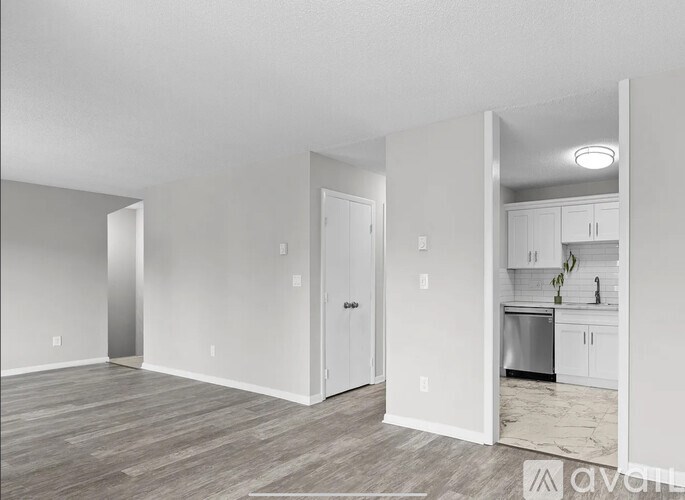 A spacious, empty room with a kitchen visible through the open door.