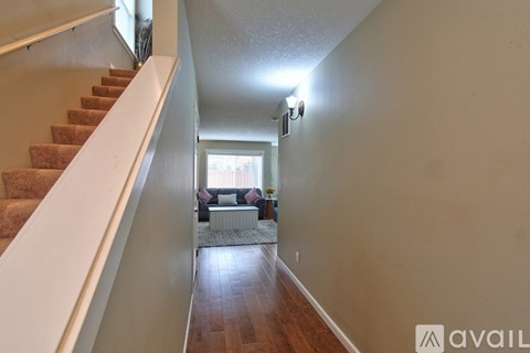 A long hallway with a staircase on the left and a living room with a couch and a coffee table on the right.