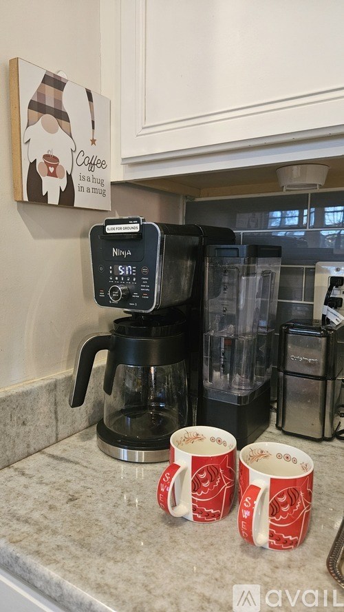Two red mugs on a counter next to a coffee maker.