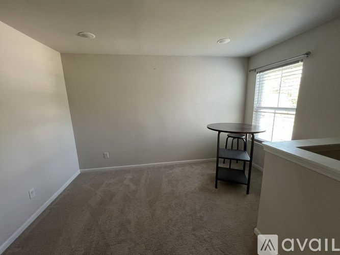 A room with a carpeted floor and a table with a chair.