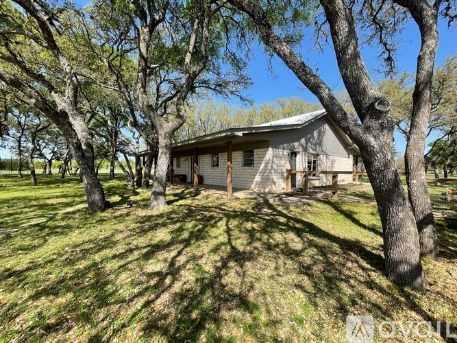 A house is surrounded by trees in a grassy area.