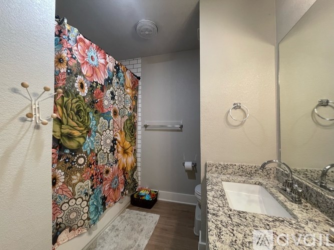 A bathroom with a floral shower curtain and a marble countertop.