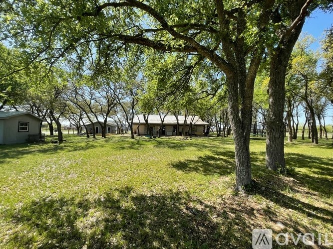 A grassy field with trees and a house in the background.