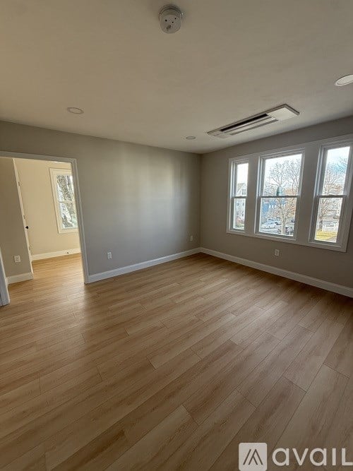 A room with wooden flooring and a window showing a view of trees and a building.