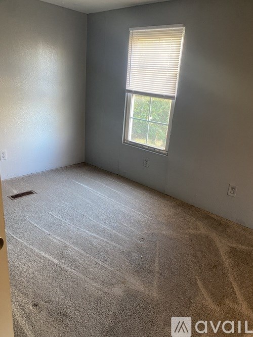 A room with a carpeted floor and a window with blinds.