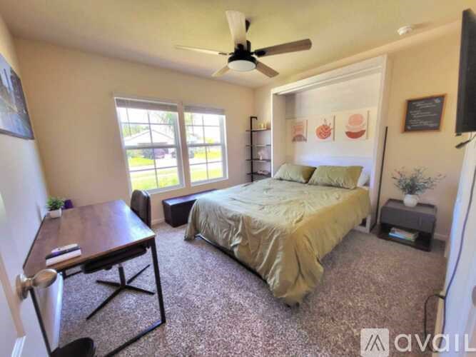 A bedroom with a bed, a desk, and a ceiling fan.