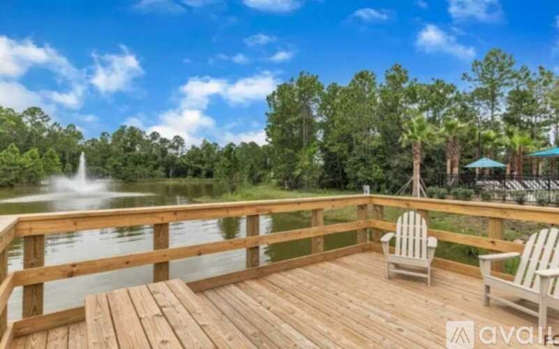 A wooden deck with two chairs and a table overlooking a lake with a fountain.
