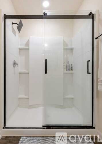 A white shower stall with a glass door and a black handle.