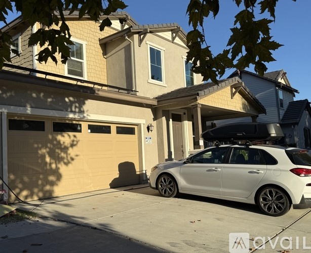A white car is parked in front of a two-story house.
