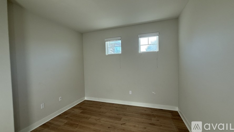 A room with wooden flooring and two windows.
