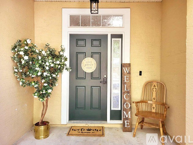 A welcoming front porch with a green door, a tree, a chair, and a welcome mat.