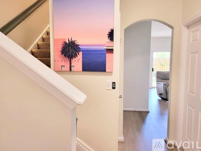 A staircase leads to a living room with a beach scene on the wall.