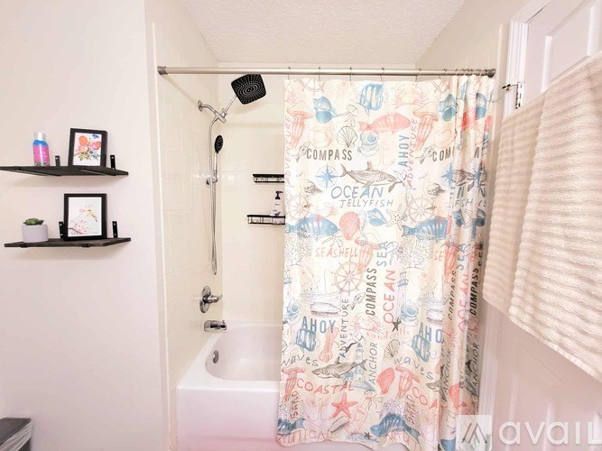 A shower curtain with ocean and compass themed designs hangs in a bathroom.