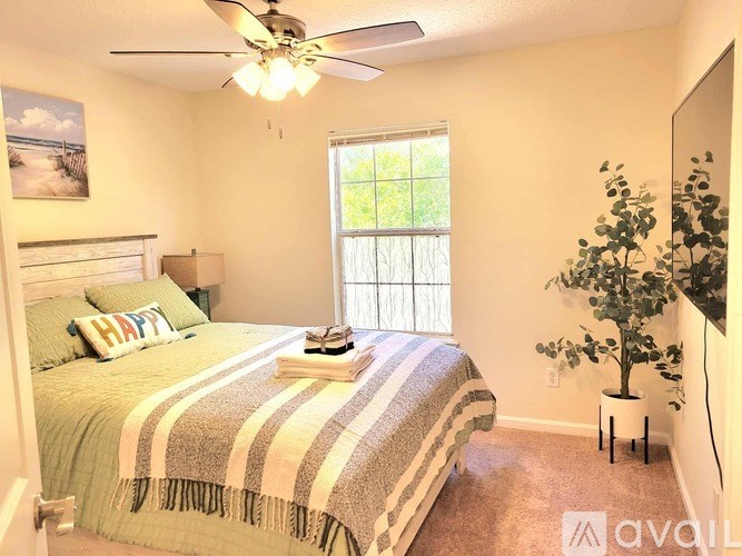 A bedroom with a bed, a ceiling fan, and a potted plant.